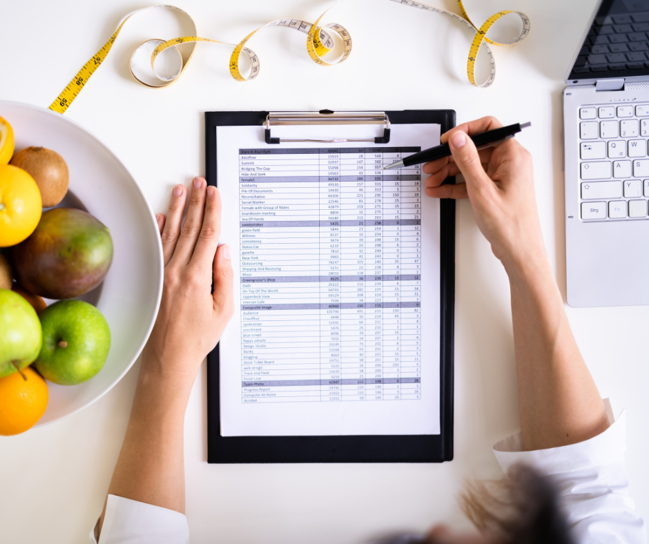 Nutritionist holding a clipboard with a diet plan, surrounded by fruits and a laptop.