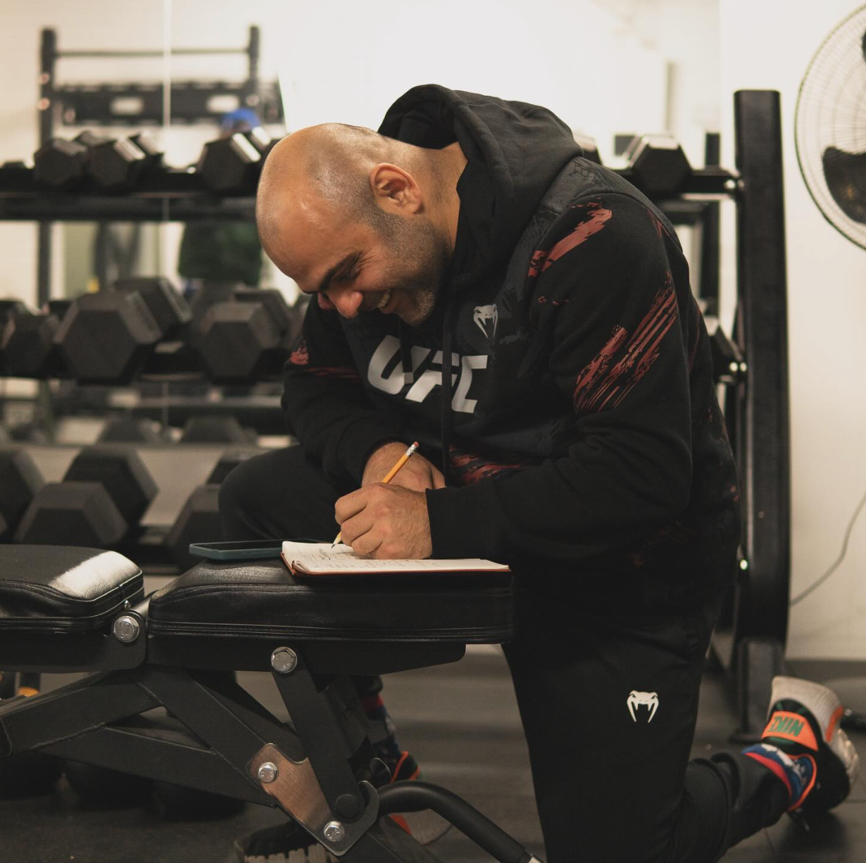 Luigi Meli (a nutritionist in Montreal) writing in a notebook on a gym bench with gym equipment in the background